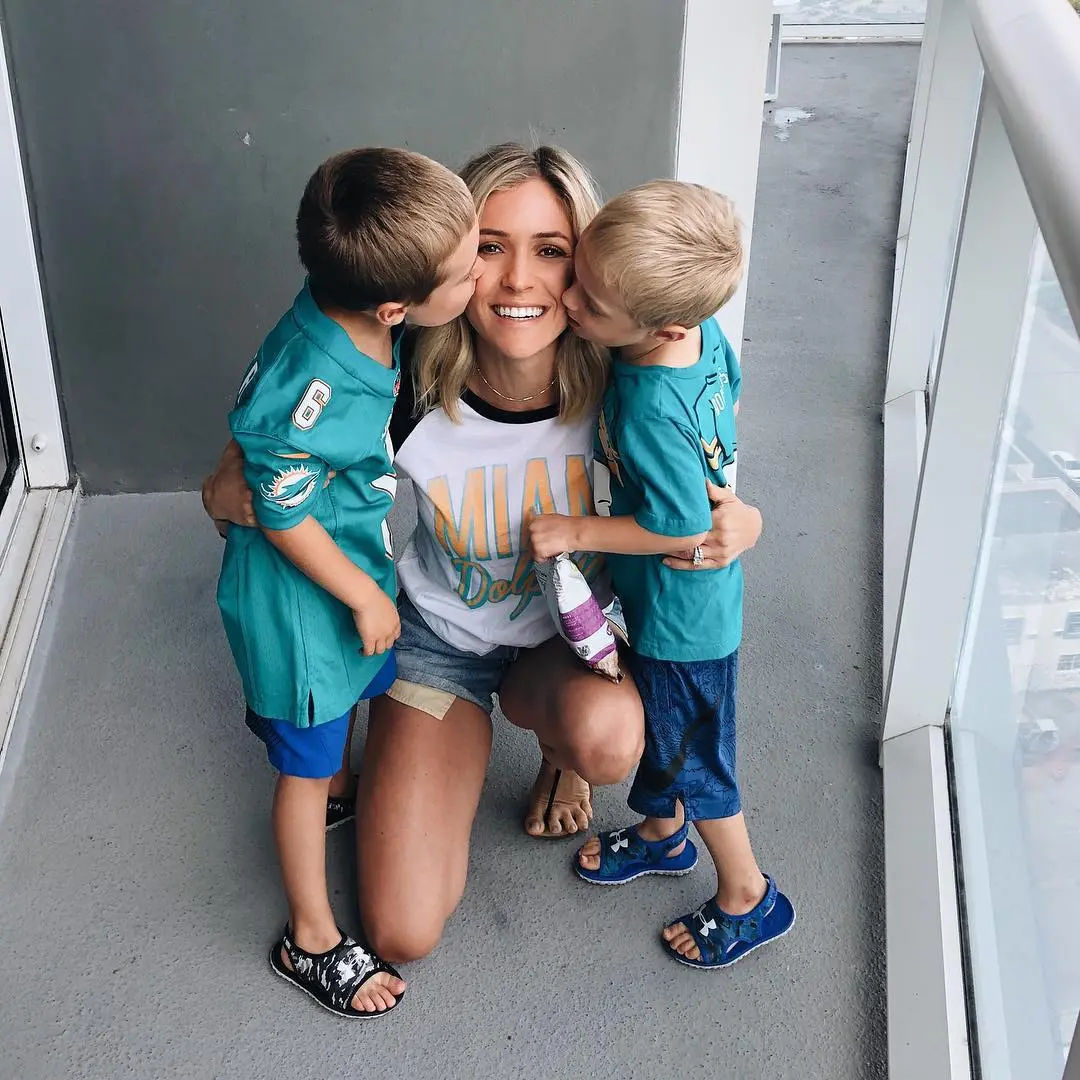 Kristin Cavallari kneeling between her two sons who are kissing her cheeks.