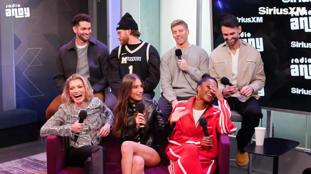 A panel of six people, three women in front and three men behind them, sitting with microphones at a 