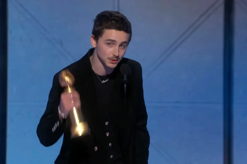 Timothée Chalamet speaking at a microphone while holding a Golden Globe award.