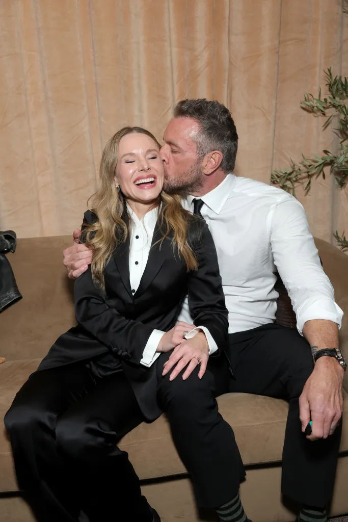 Kristen Bell and Dax Shepard share a kiss while seated on a couch.