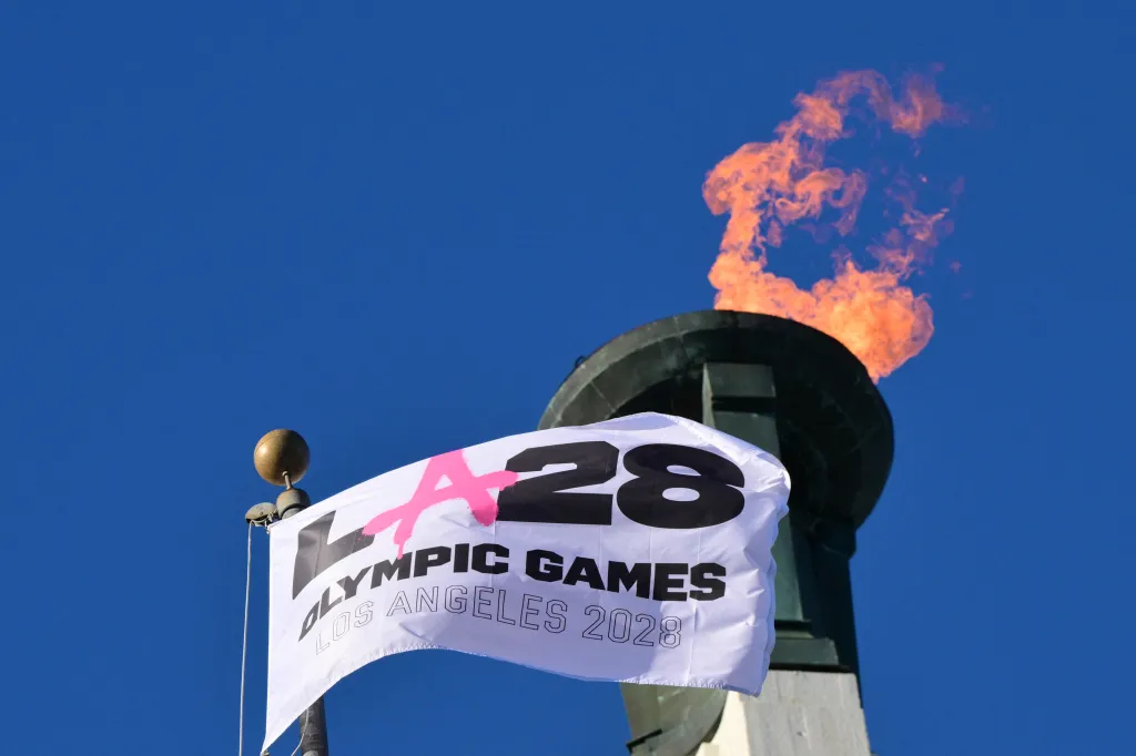 The LA28 Olympic Games cauldron is lit, with a white flag displaying the 