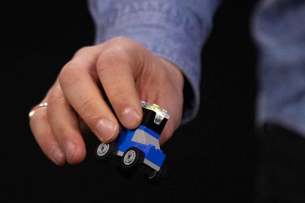 A person holding a blue, black, and gray LEGO vehicle with a smart brick attached.
