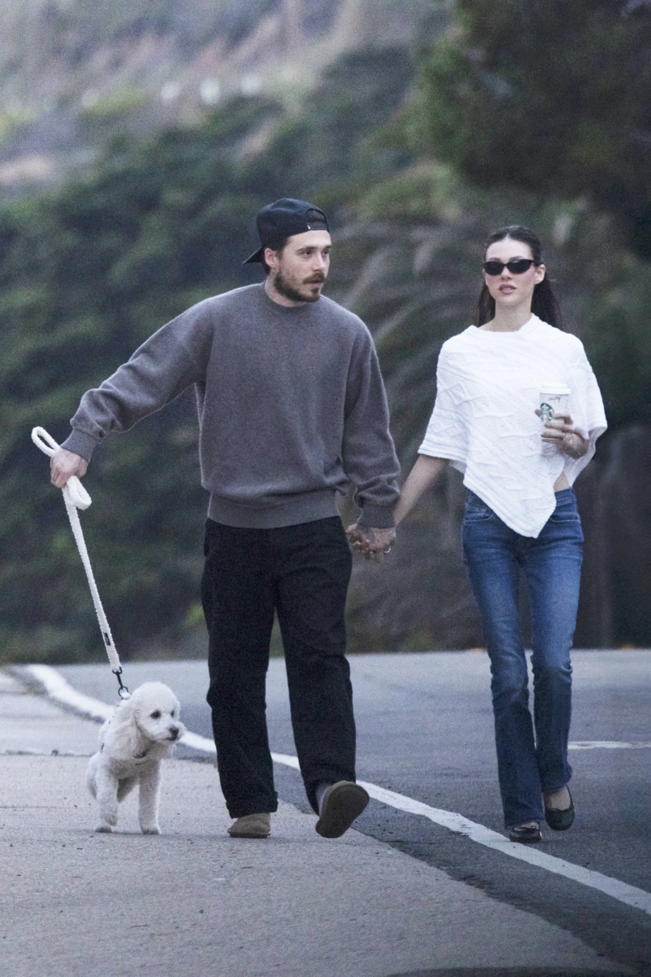 Brooklyn Beckham and Nicola Peltz Beckham holding hands and walking their white rescue dog in Malibu.
