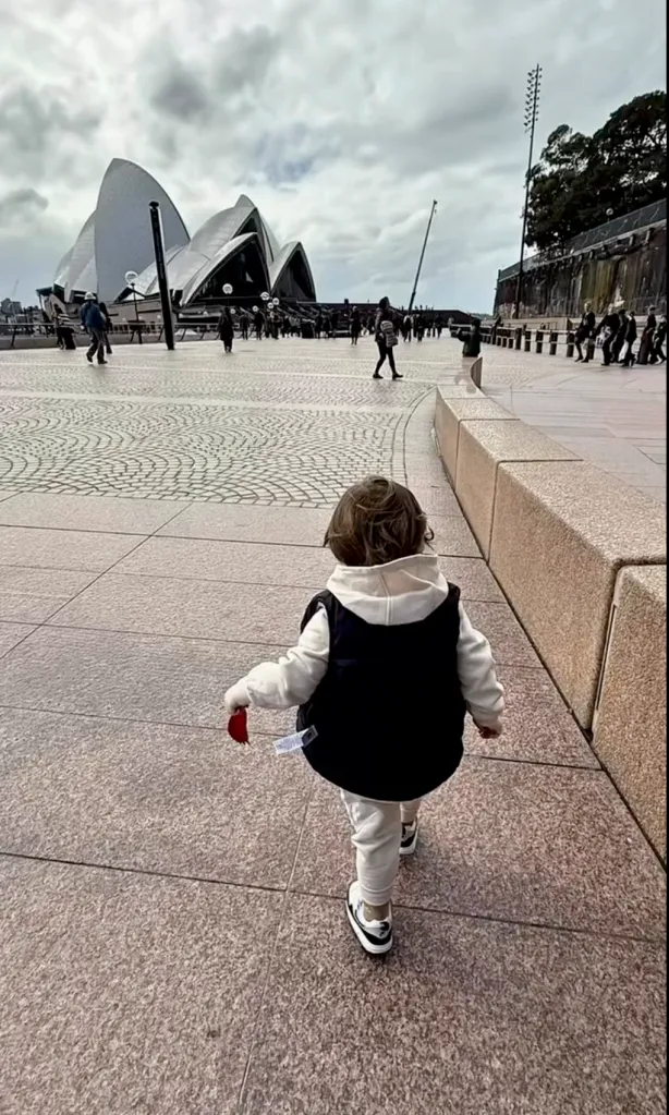 Lindsay Lohan's son walking away from the camera with the Sydney Opera House in the background.