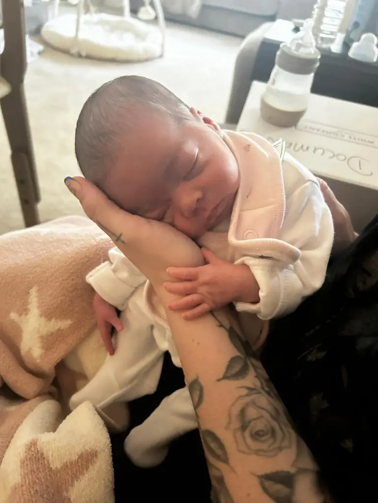 A baby sleeping on a tattooed arm.