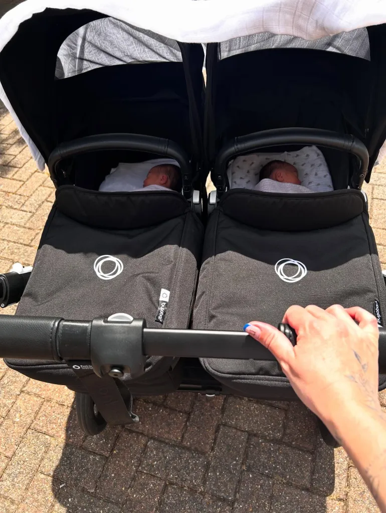 A person pushing a twin stroller with two babies inside.