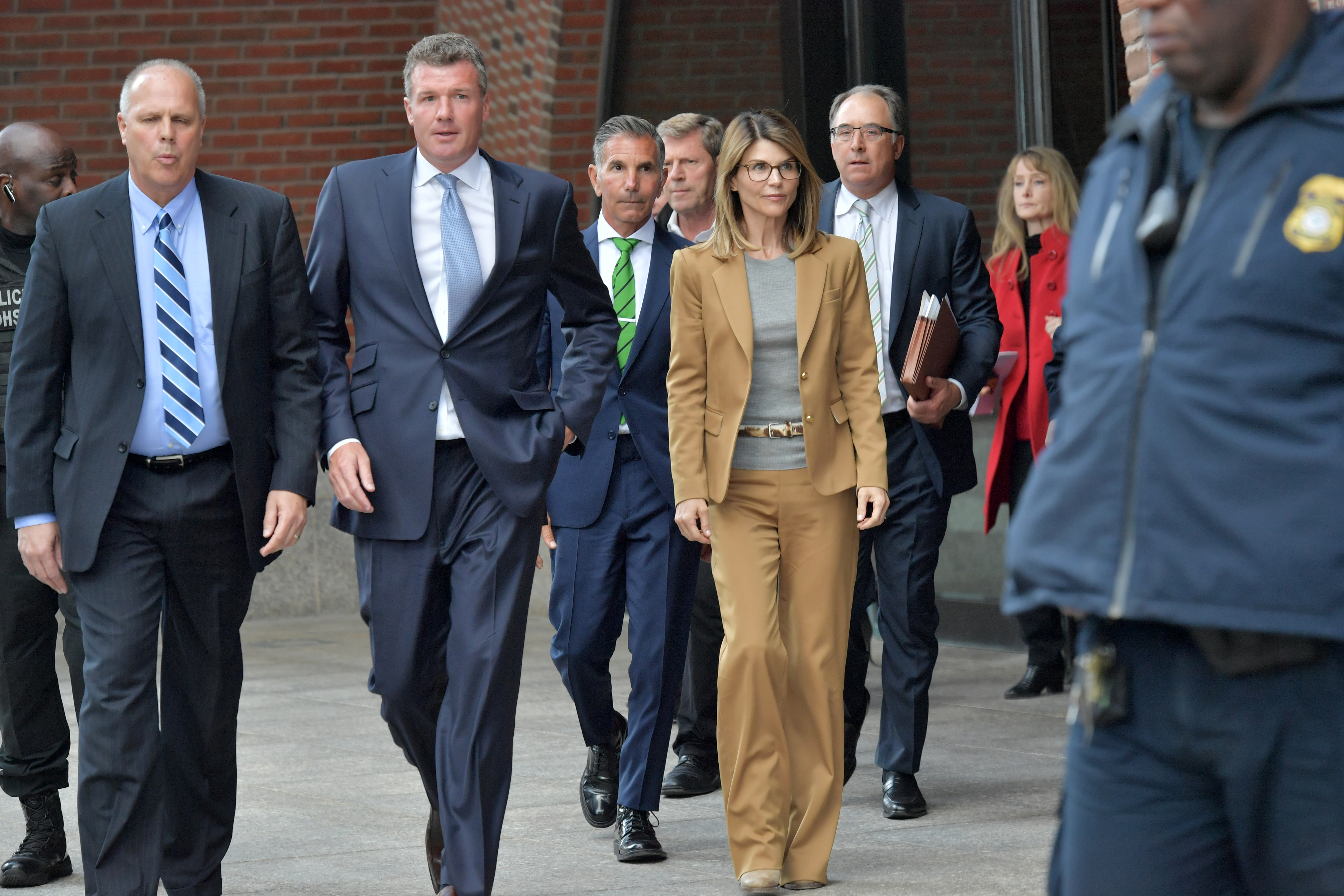 Lori Loughlin leaving the John Joseph Moakley U.S. Courthouse in Boston in a tan pantsuit and glasses, surrounded by men in suits.