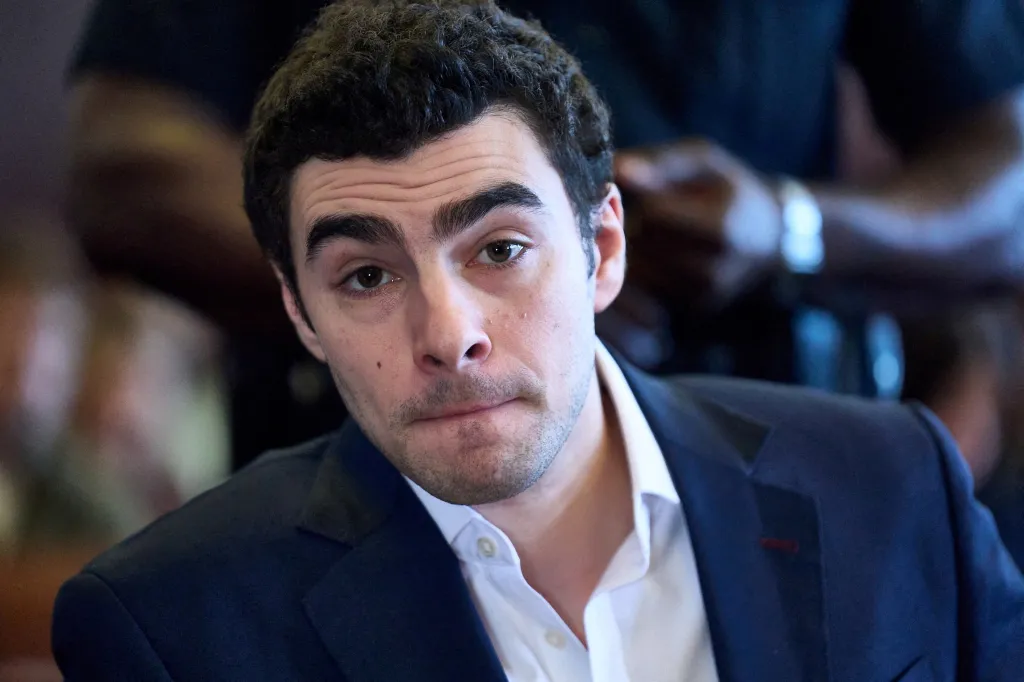 Luigi Mangione in a navy suit and white shirt looks at the camera during a court hearing.