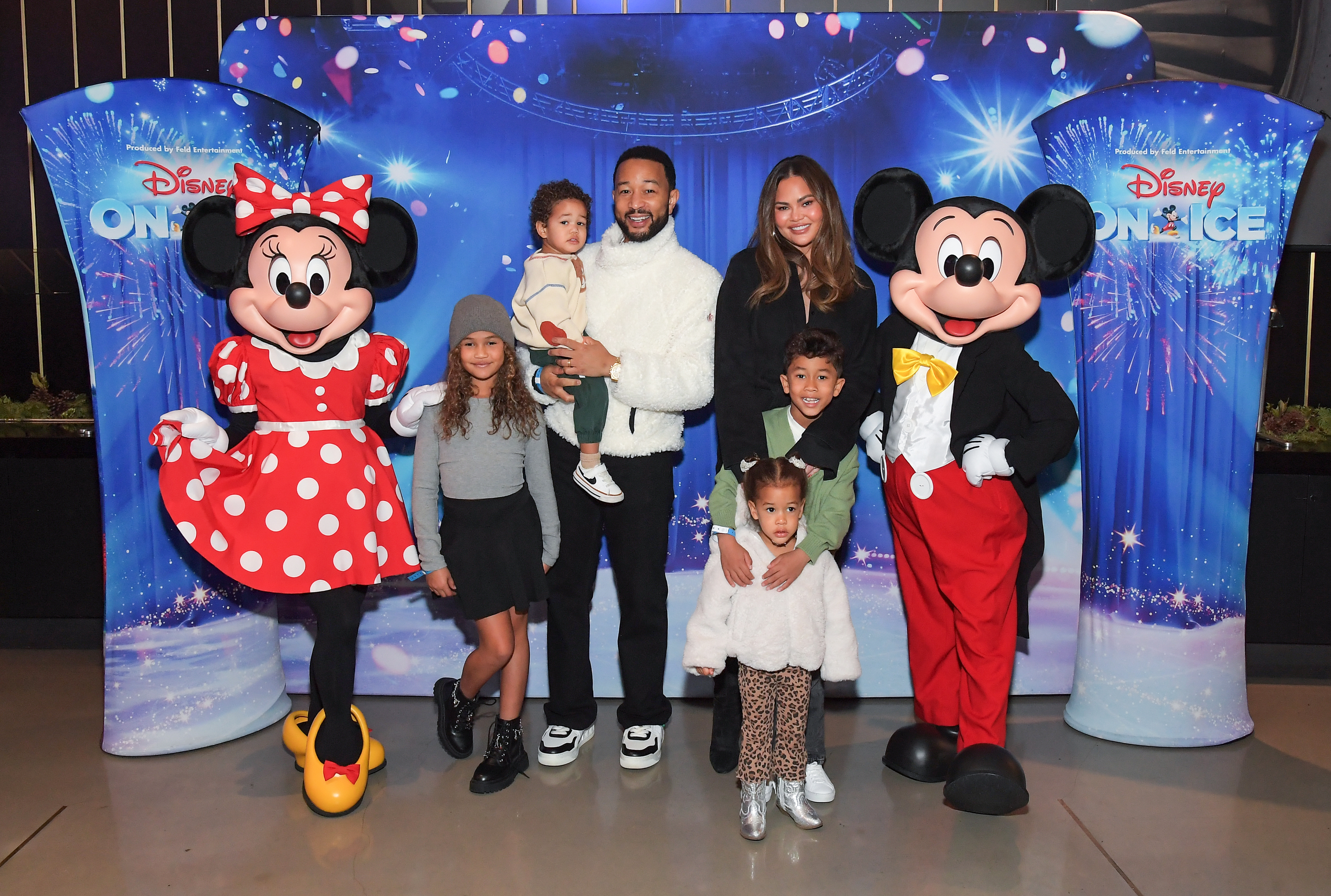 John Legend, Chrissy Teigen, and their four children posing with Minnie and Mickey Mouse mascots.