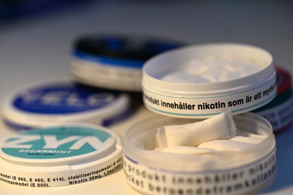 Several open and closed containers of nicotine pouches, with Swedish warning labels visible.
