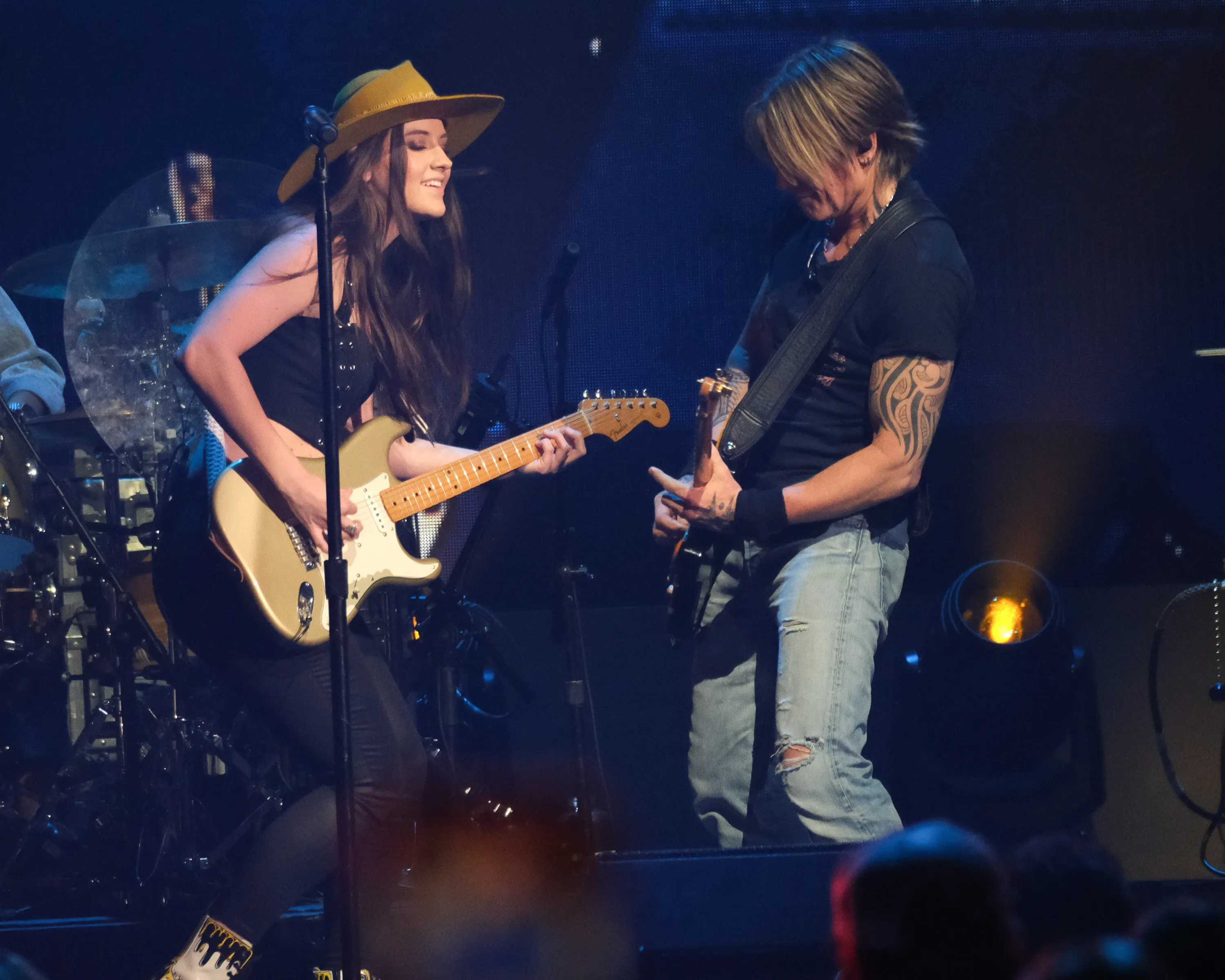 Maggie Baugh and Keith Urban performing on stage, both playing guitars.