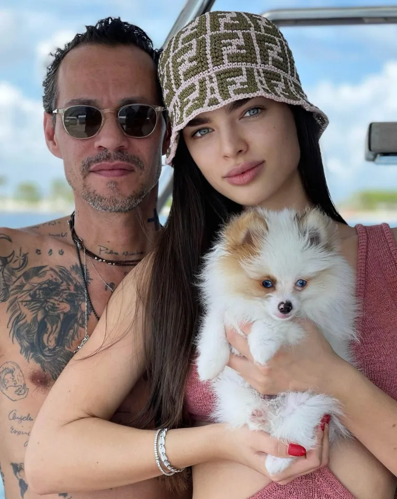 Marc Anthony and Nadia Ferreira posing with a small dog.