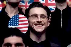 Timothee Chalamet as Marty Supreme wearing glasses, smiling, with a round American flag sign.