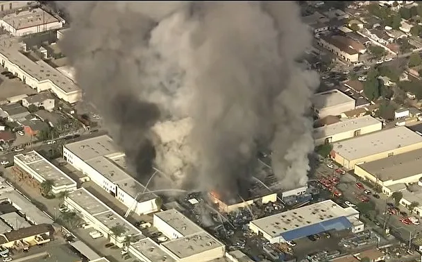 Aerial view of a massive fire engulfing buildings in South El Monte, producing thick plumes of dark smoke.