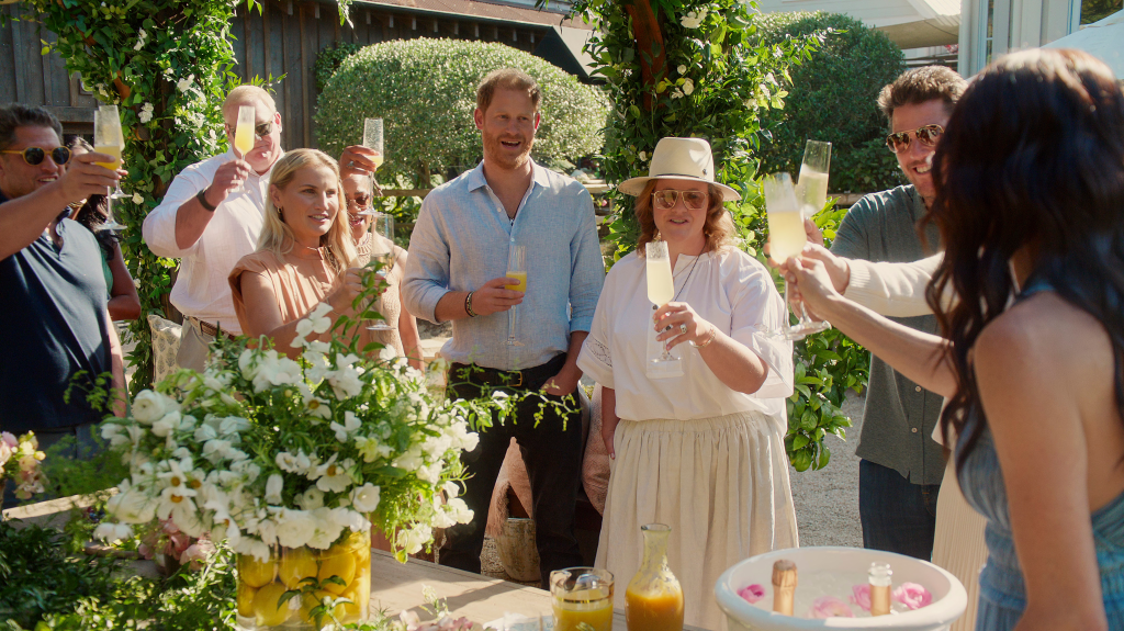 From left, Matt Cohen, in a grey t-shirt, Brian Kocinski, in a white shirt, Heather Dorak, in a peach dress, Doria Ragland, Prince Harry, in a blue shirt and black pants, Genevieve Hillis, in a white shirt, cream skirt and cream hat,Julian Zafjen, in a grey shirt and black pants,and Meghan, Duchess of Sussex, in a blue dress, in a group toast.