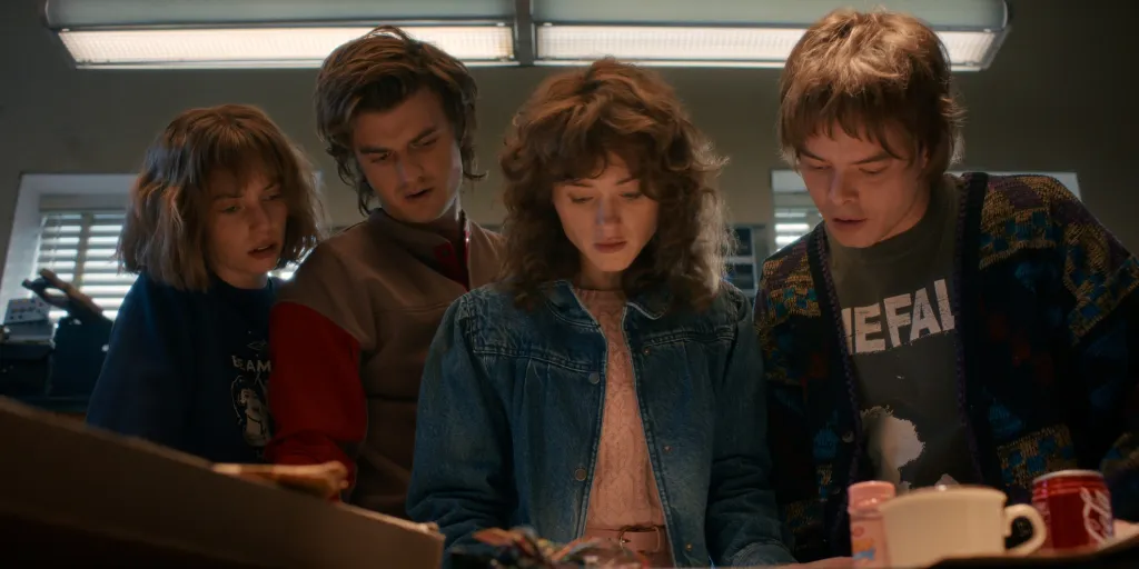 Maya Hawke, Joe Keery, Natalia Dyer, and Charlie Heaton from *Stranger Things* looking down.