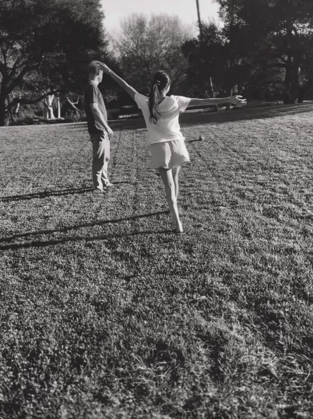 Meghan Markle dancing on the grass with Prince Harry in the background.