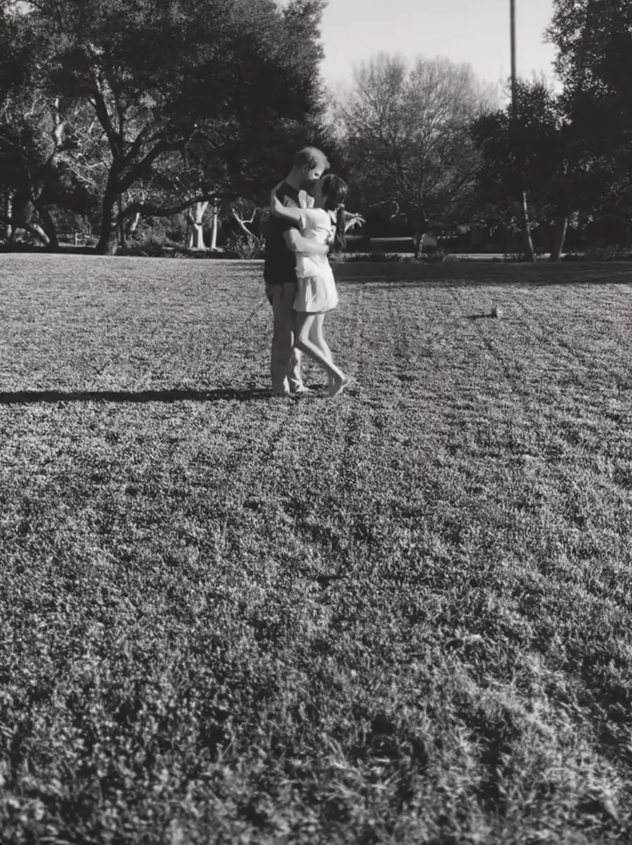 Black and white photo of Meghan Markle and Prince Harry dancing barefoot in a field.