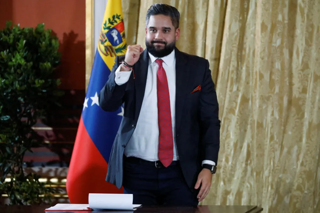 Nicolas Maduro Guerra gestures with a fist while standing in front of a Venezuelan flag.