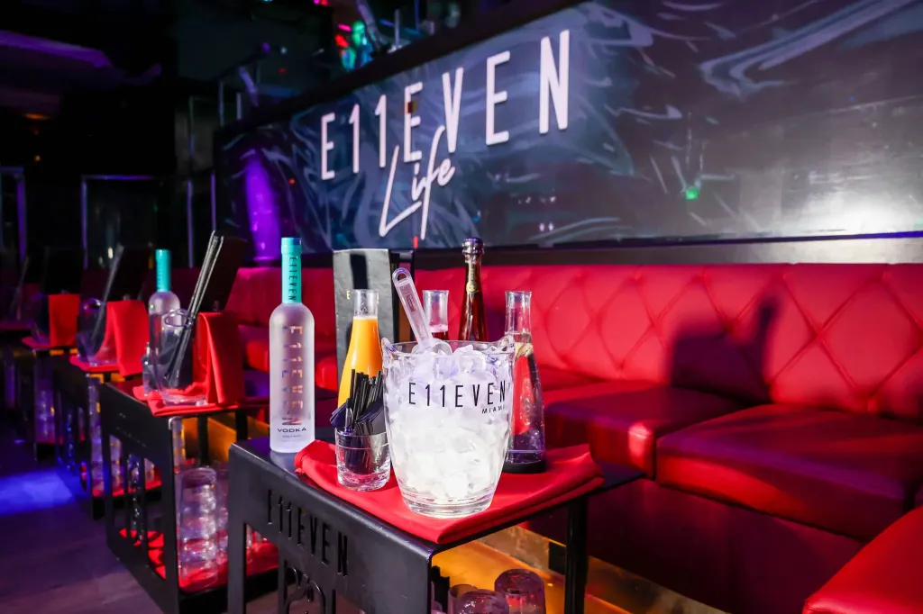 Bottles of liquor and an ice bucket on a table with a red couch in the background at Miami's Club E11EVEN.