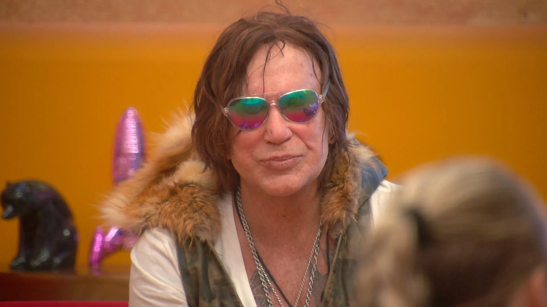 Mickey Rourke wearing iridescent sunglasses and a fur-lined vest.