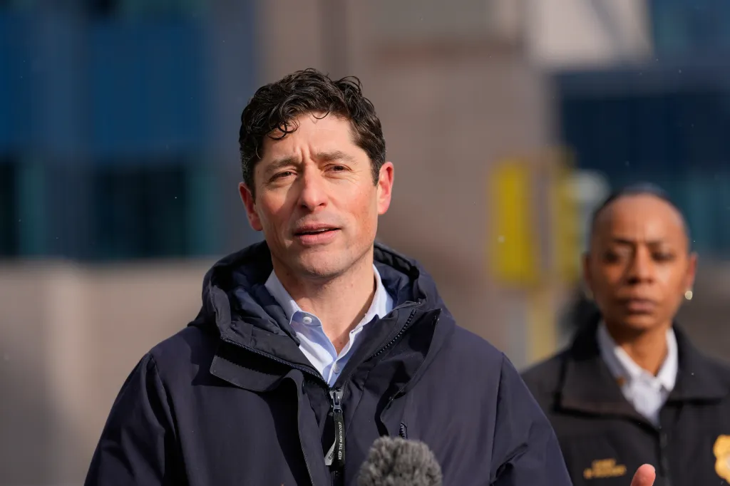 Minneapolis Mayor Jacob Frey speaks during a news conference, with another person out of focus in the background.