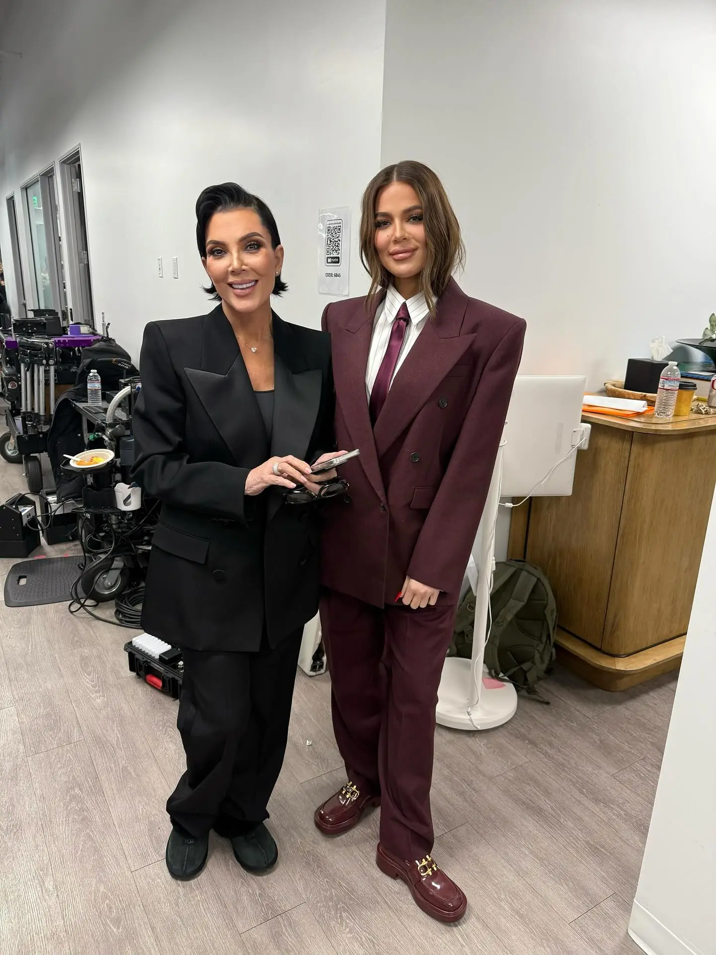 Kris Jenner in a black pantsuit next to Khloé Kardashian in a burgundy pantsuit.