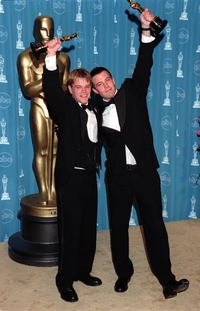 Matt Damon and Ben Affleck holding their Oscars above their heads.