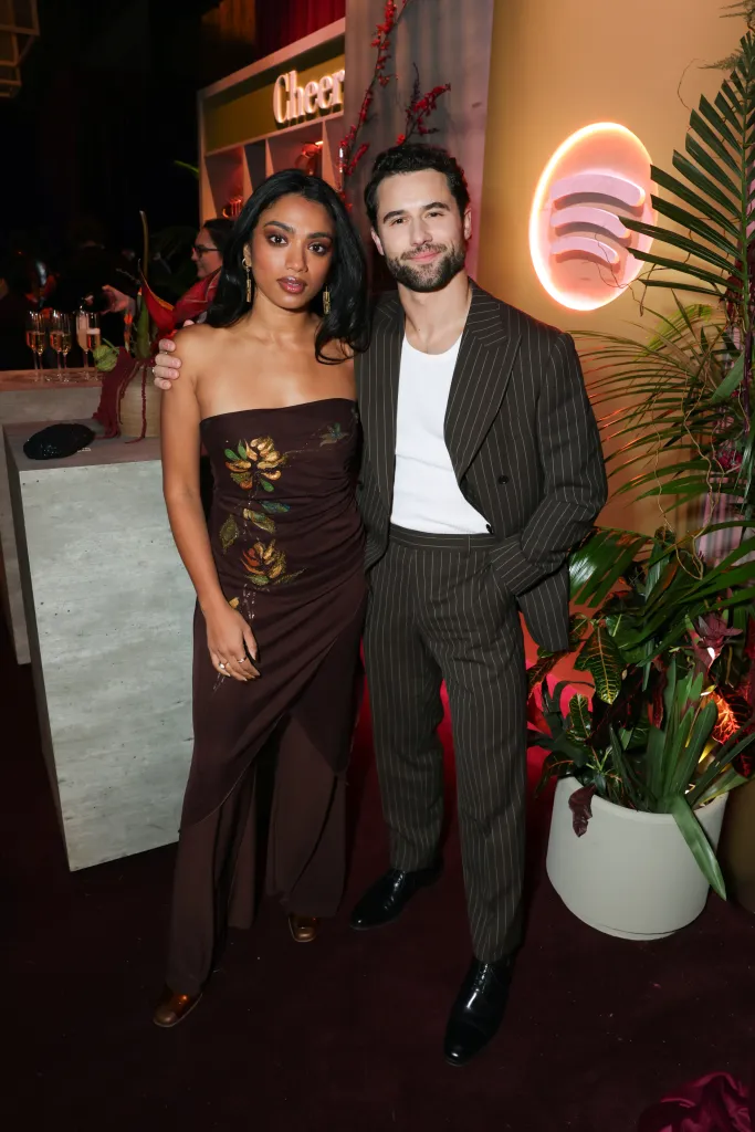 Nadine Bhabha and Robbie G.K. smiling at the camera, Bhabha in a strapless brown dress with gold floral accents, and G.K. in a pinstriped suit with a white undershirt.