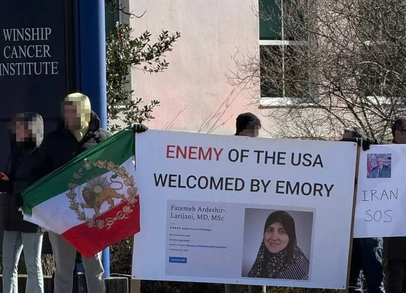 Protestors hold signs outside the Winship Cancer Institute, one with the Iranian flag and another reading