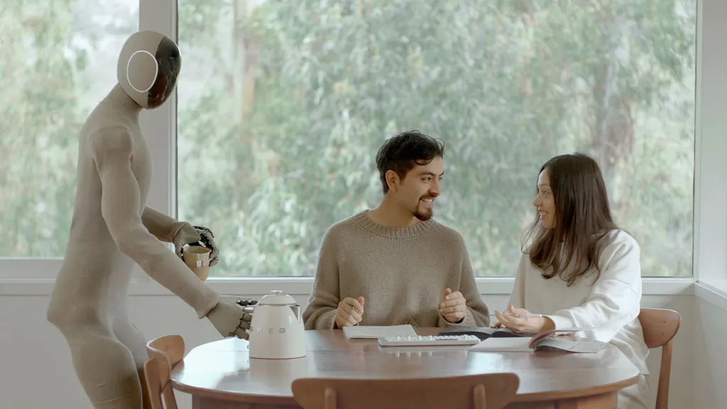 A humanoid robot serves coffee to two people sitting at a table.
