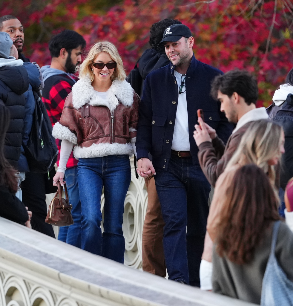 Sydney Sweeney and Scooter Braun walking hand-in-hand across Bow Bridge in Central Park, surrounded by other people.