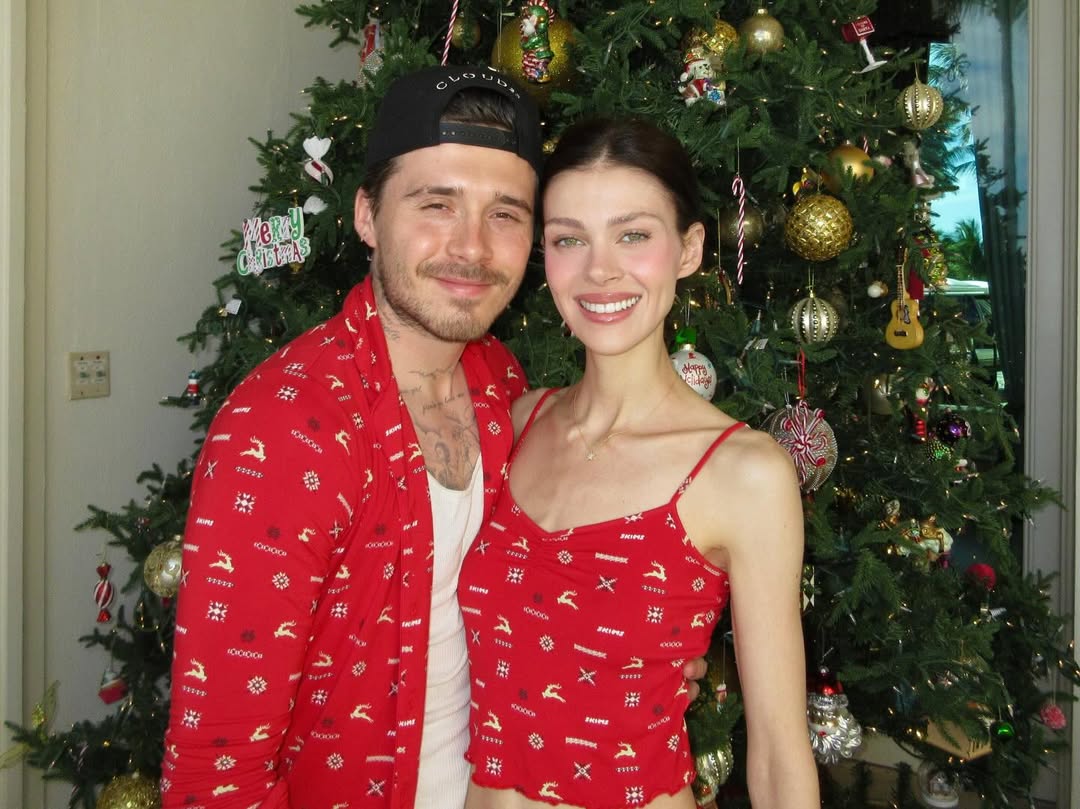 Brooklyn Beckham and Nicola Peltz Beckham in matching red Christmas outfits in front of a Christmas tree.