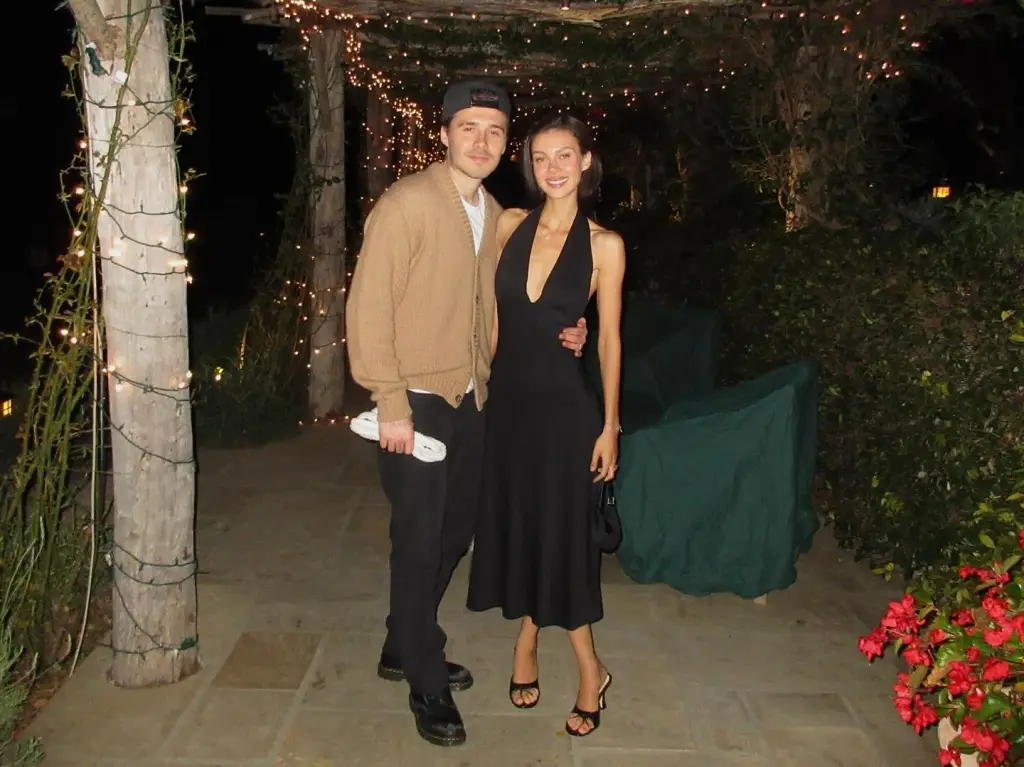 Nicola Peltz and Brooklyn Beckham standing together at night outdoors.