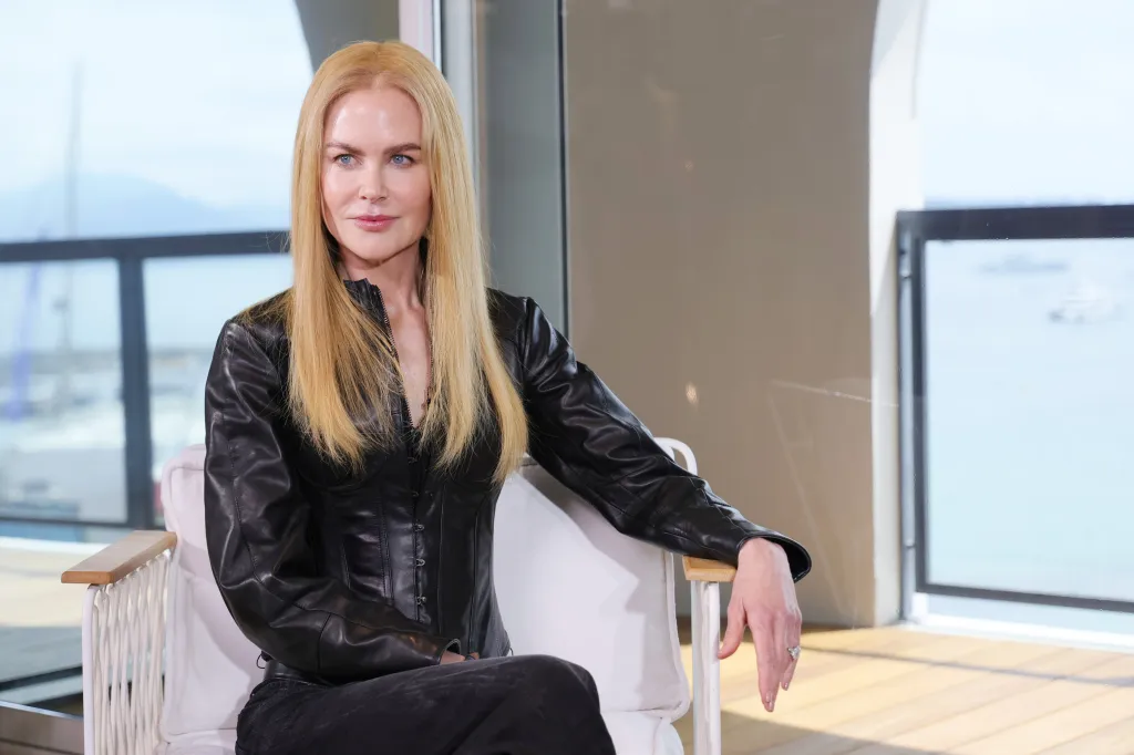 Nicole Kidman in a black leather outfit, sitting in a white armchair.