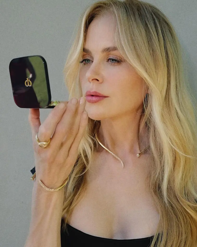 Nicole Kidman applying lipstick while holding a compact mirror.
