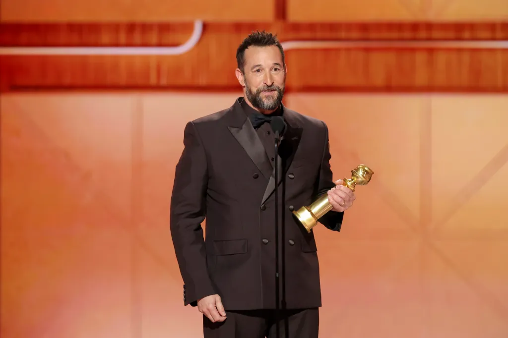 Noah Wyle holding a Golden Globe award on stage.