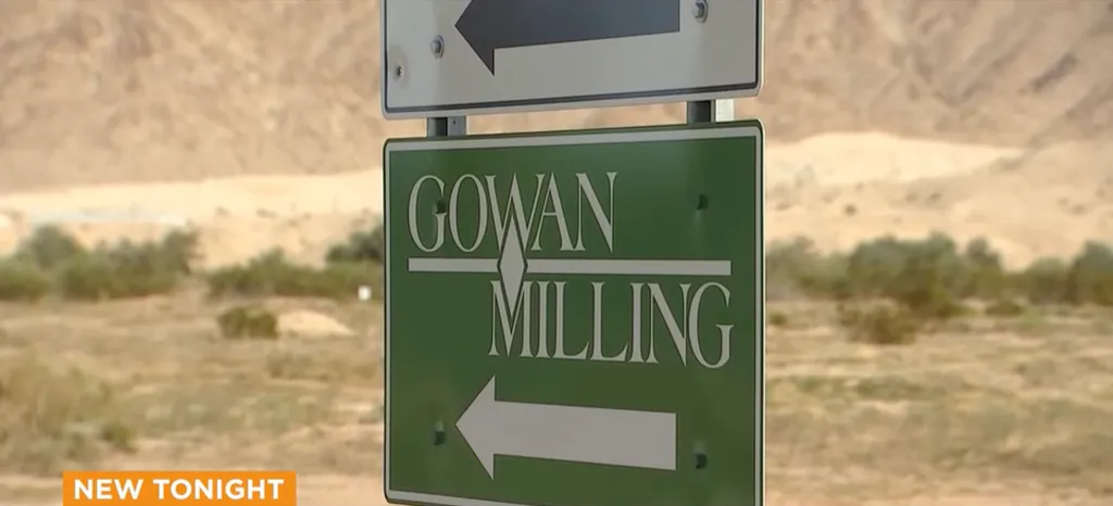 A green sign for Gowan Milling with an arrow pointing left, against a desert backdrop.