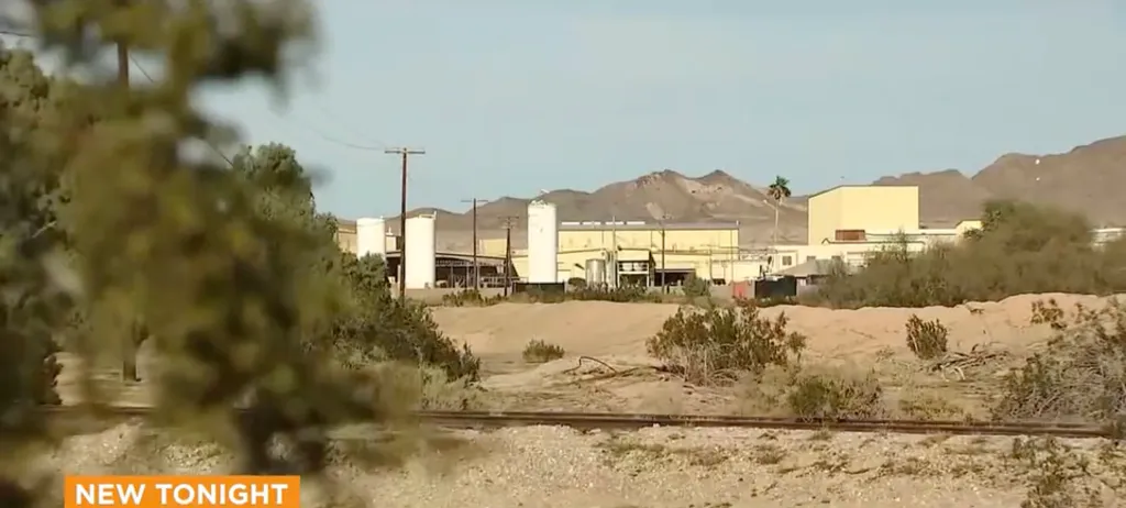 A chemical manufacturing facility with multiple buildings and storage silos, located in a desert landscape.