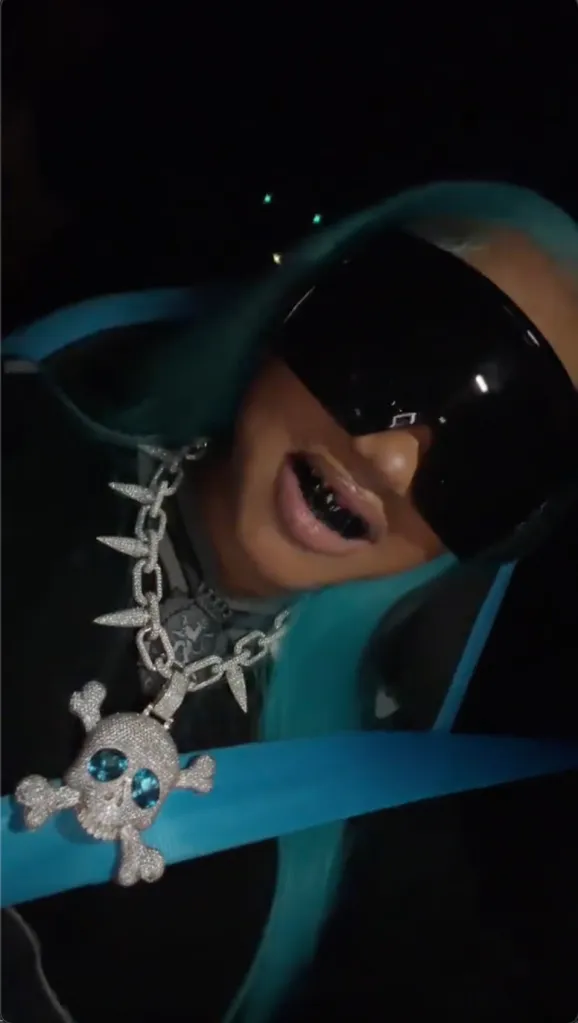 North West in a car wearing dark sunglasses, a diamond skull necklace, and a grill on her teeth.