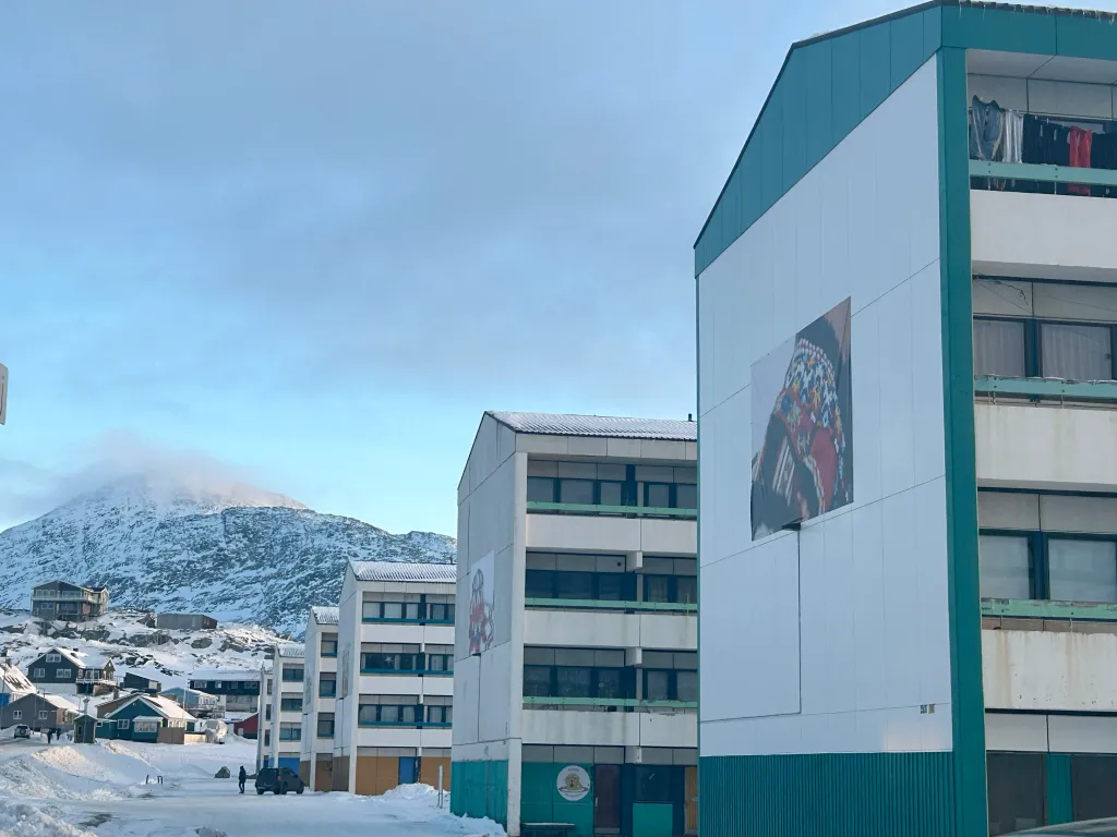 Several apartment buildings in Nuuk, Greenland, with a snowy mountain and smaller houses in the background.