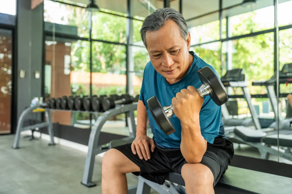 An older man weight training with a dumbbell in a gym.