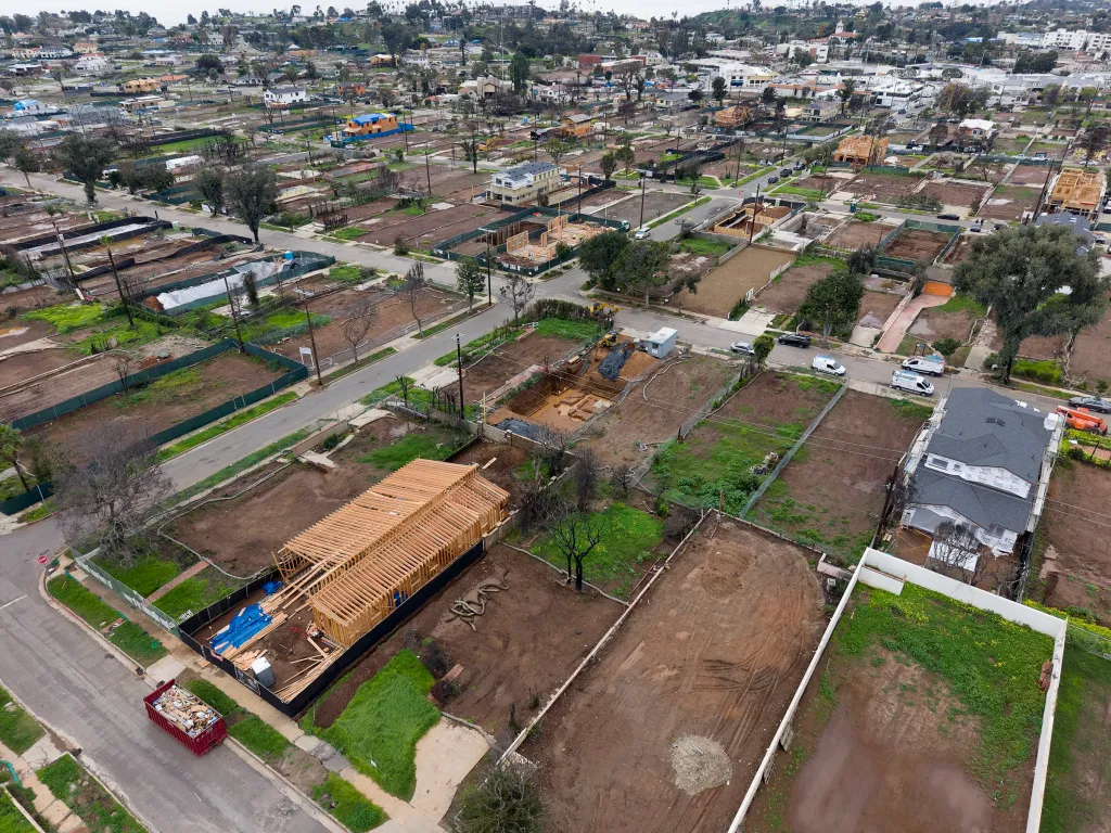 Aerial view of a neighborhood in Pacific Palisades, California, showing some homes rebuilt after a fire and many vacant plots.