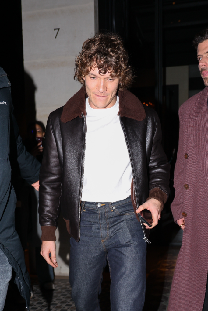 Connor Storrie in a Sandro leather jacket, white tee, and bootcut jeans.