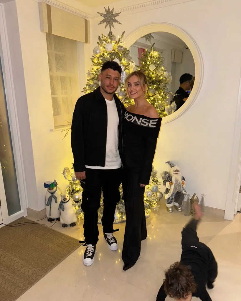 Perrie Edwards and Alex Oxlade-Chamberlain posing in front of a Christmas tree as their baby crawls on the floor.