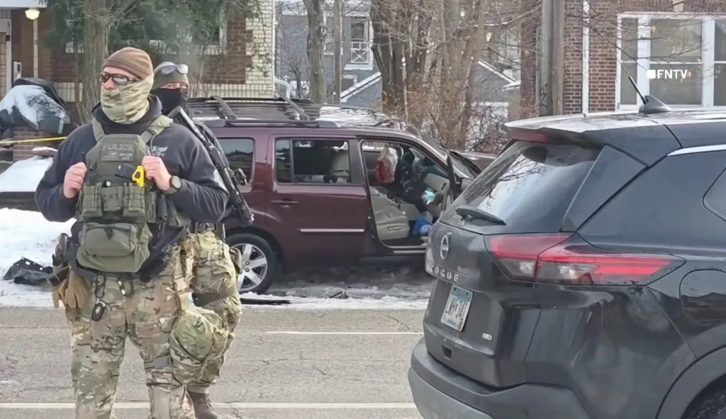 Two federal agents in tactical gear with a red SUV with an open door and a black SUV in the foreground.