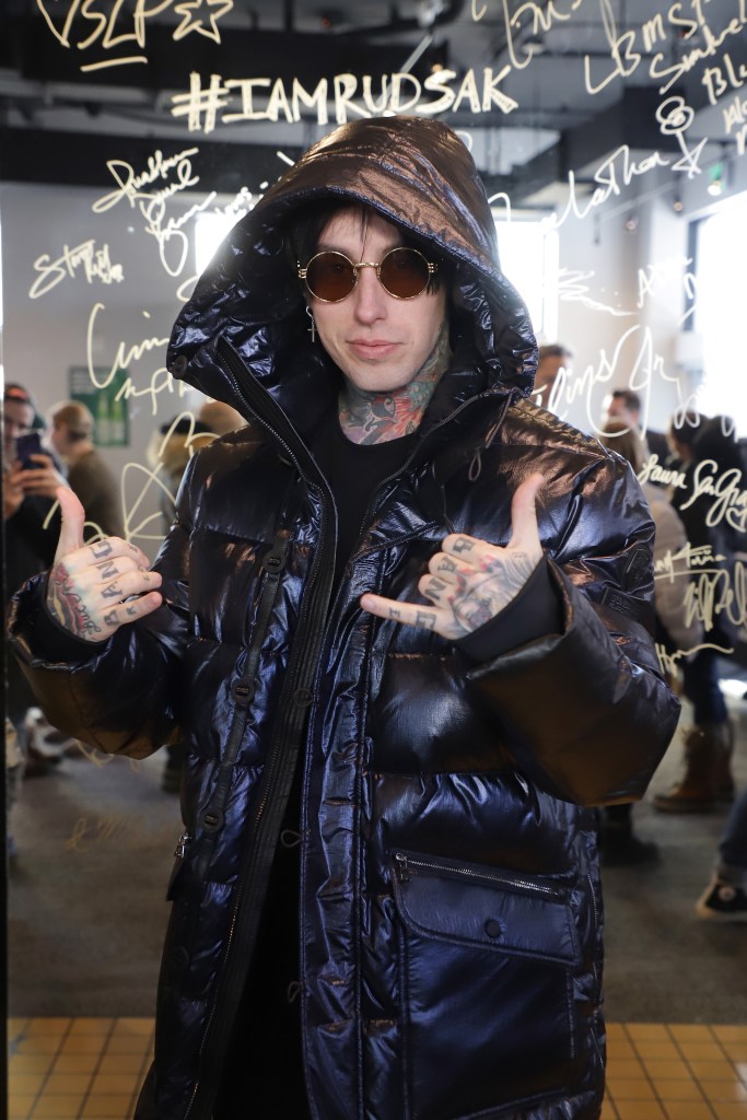 Ronnie Radke in a black puffer jacket and sunglasses, making a shaka sign with both hands.