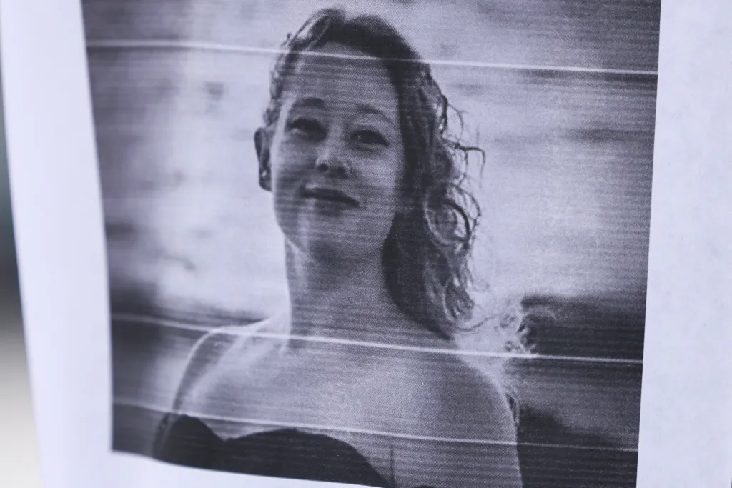 A black and white photograph of Renee Nicole Good, with horizontal scanner lines, displayed near a makeshift memorial.