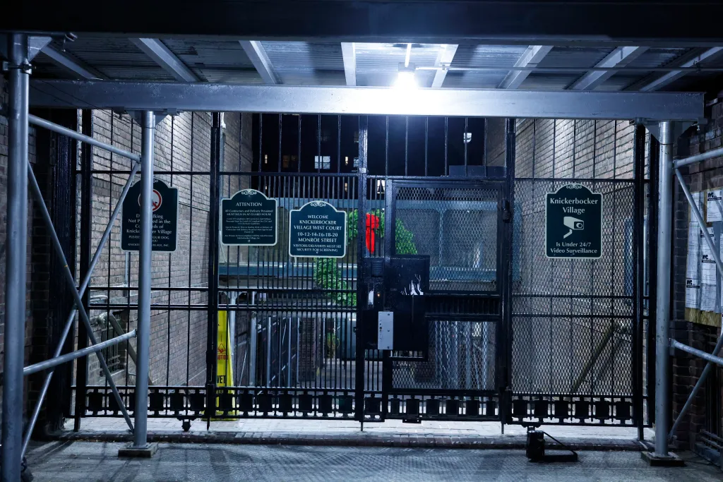 Entrance to Knickerbocker Village West Court on Monroe Street, with construction scaffolding and multiple signs, one stating 