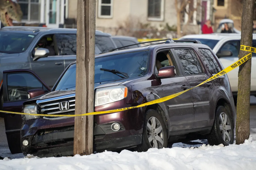 A maroon SUV with a bullet hole in its windshield and front-end damage, wrapped in yellow police tape, after a shooting in Minneapolis.